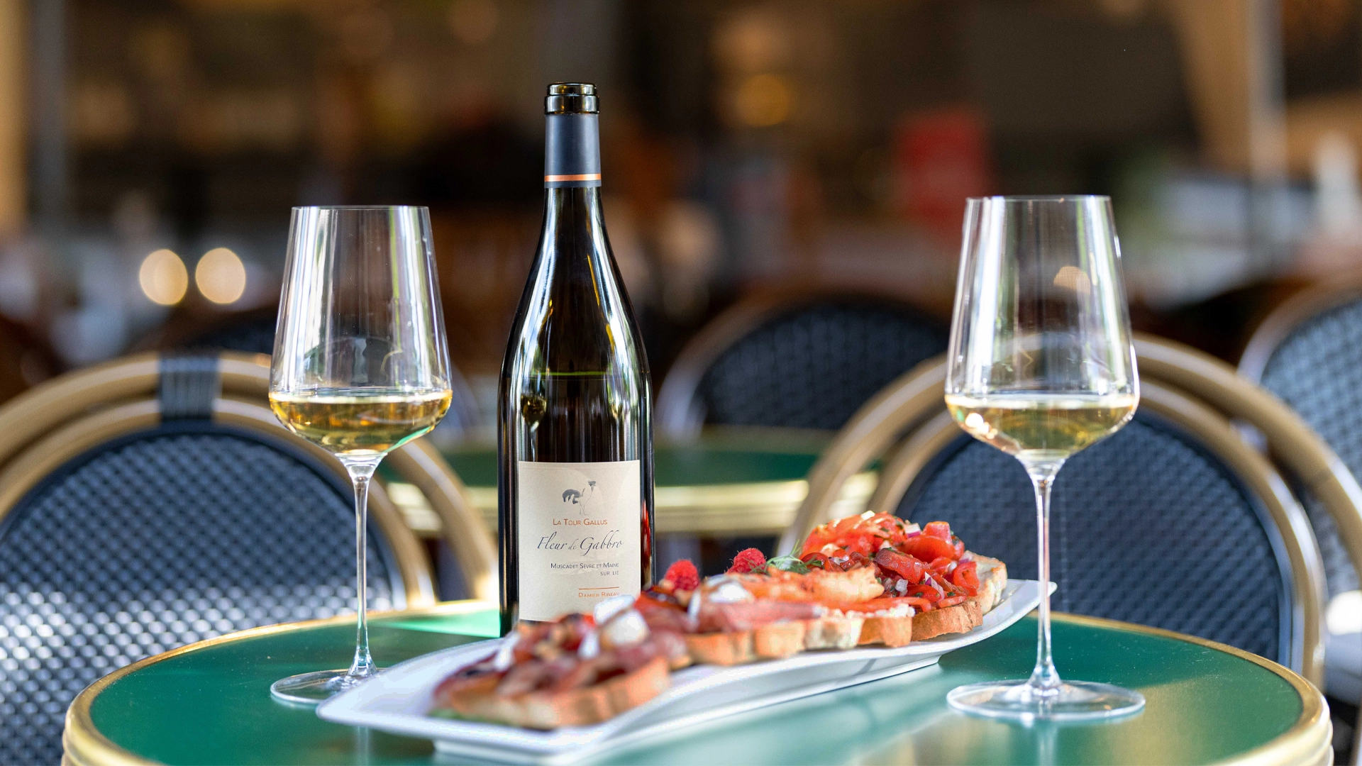 Muscadet Sur Lie Fleur de Gabbro van wijnhuis La Tour Gallus (Frankrijk) met twee wijnglazen en amuses op een terras. 