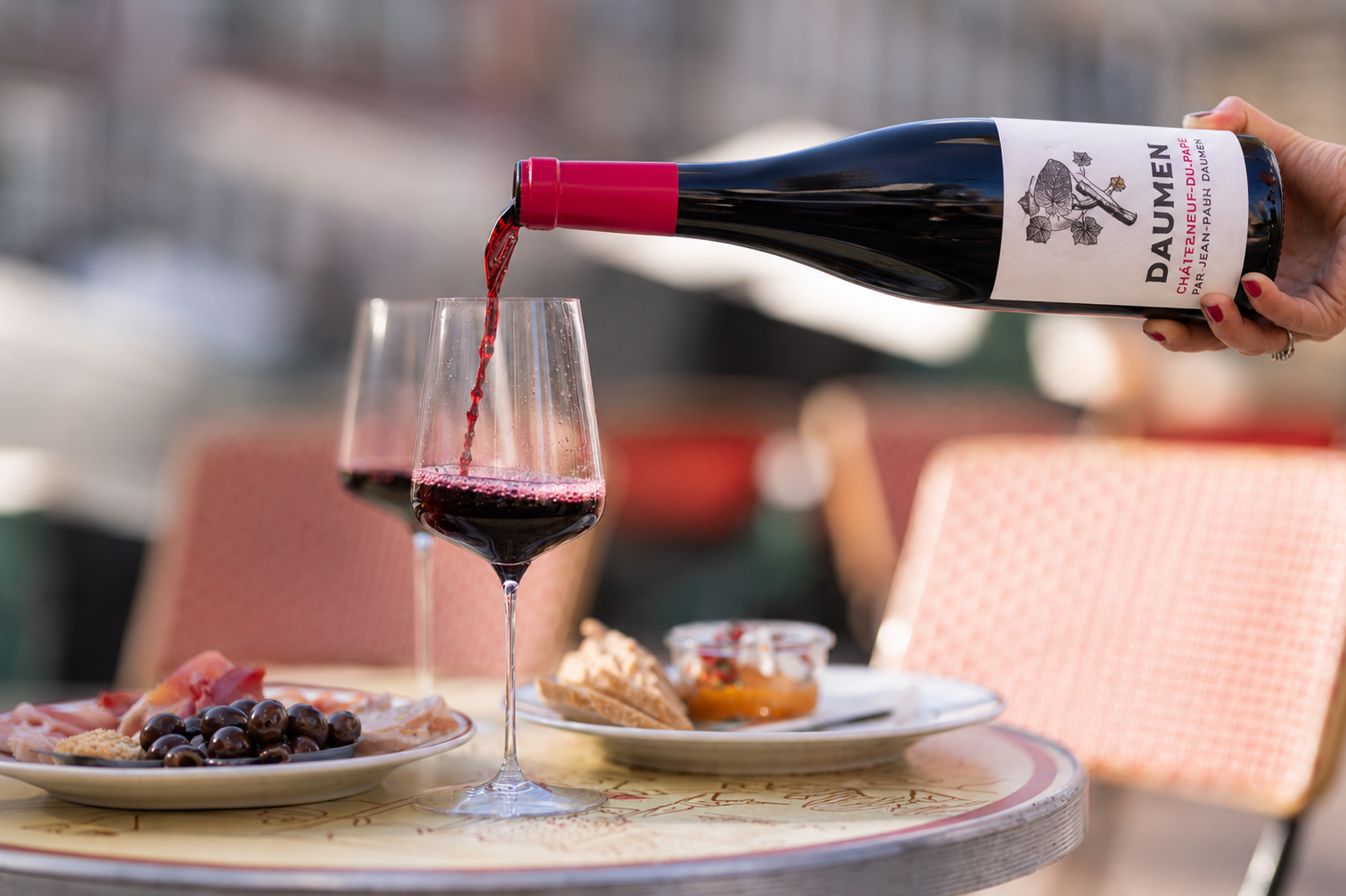 Een fles Jean Paul Daumen Chateauneuf-du-Pape Rouge wordt ingeschonken op terras met charcuterie op tafel